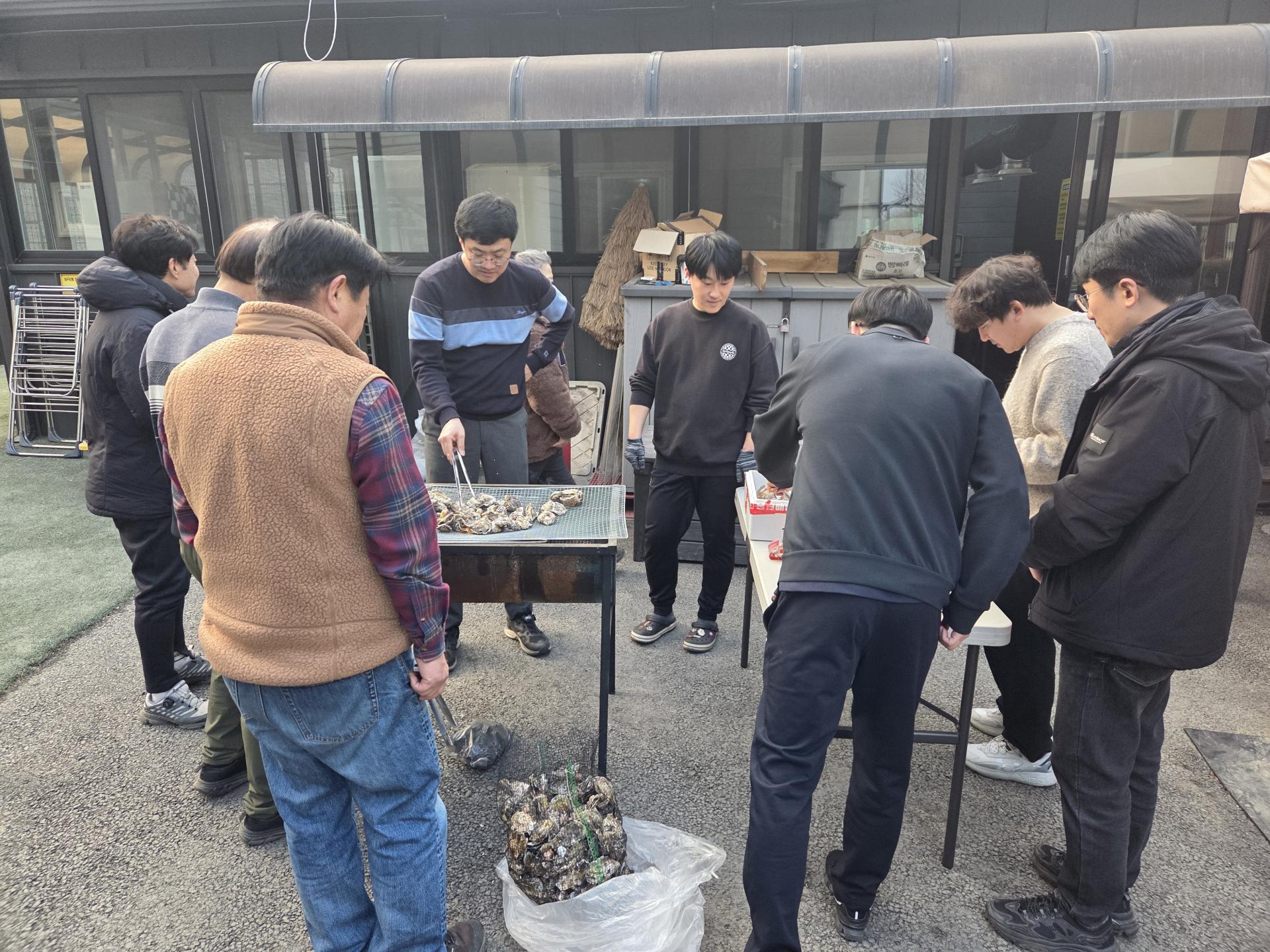 야외 테이블에서 굴을 구우며 담소하는 직원들